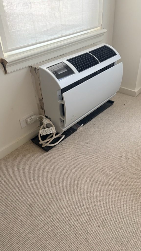 An air conditioning unit set into the wall beneath a window.